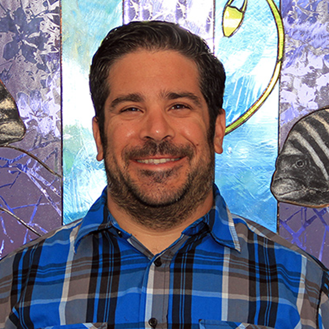 Photo of Dr. Matt Ajemian, Associate Research Professor at FAU Harbor Branch Oceanographic Institute. Man smiling with a plaid black and blue shirt on.